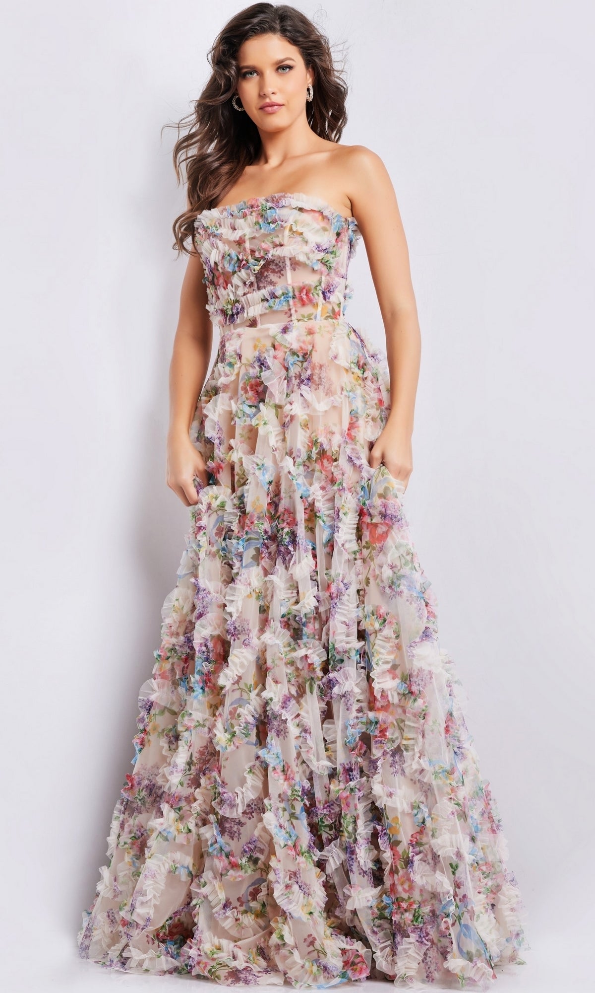 A woman poses against a plain white background wearing the Jovani Strapless Long Print Prom Dress 38650, featuring a colorful floral pattern and sheer bodice.